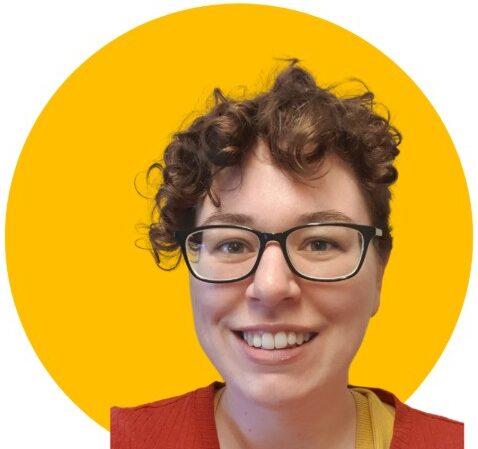 Alice, a white woman in her late 30s, is smiling broadly at the camera. She has short curly hair and is wearing glasses and a bright orange top.