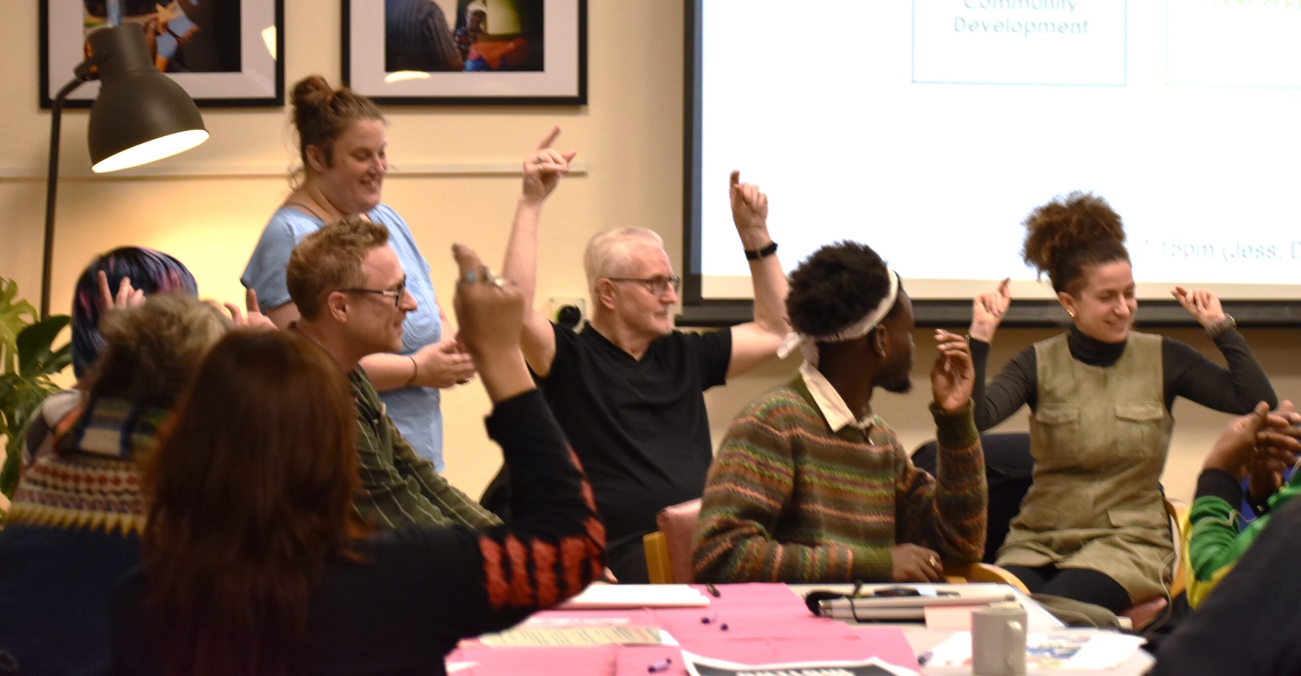 a diverse group of people sitting behind tables at a meeting are making appreciate gestures by finger snapping instead of clapping