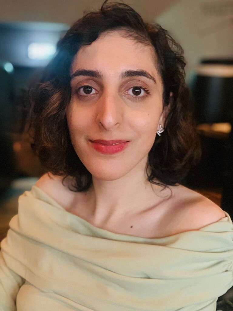 Celina is a young woman is smiling with dark curly hair and brown eyes wearing a green off the shoulder top.