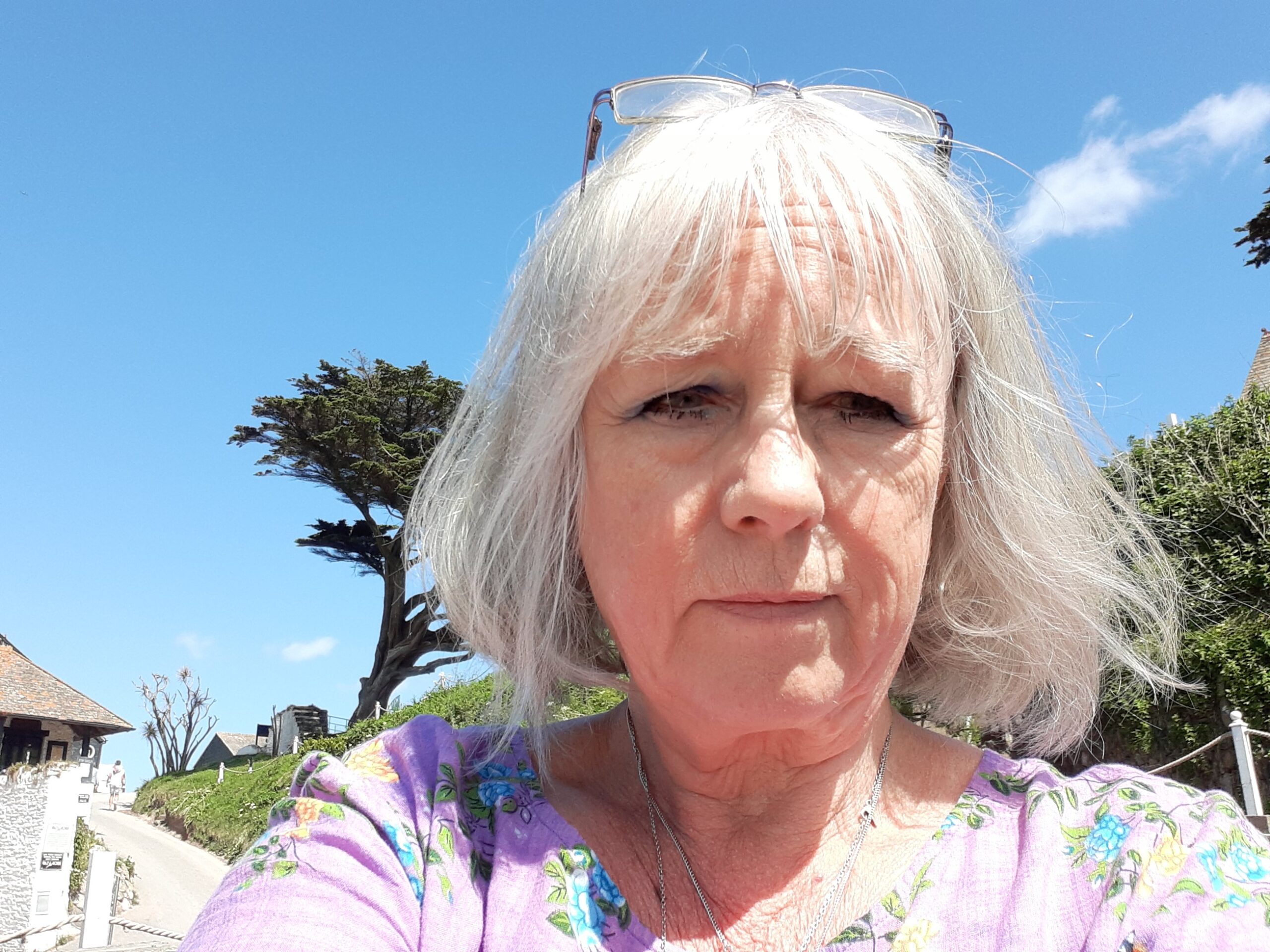 Ruth is grey haired and has sunglasses on her head, shown against the blue sky of her favourite place in Devon.