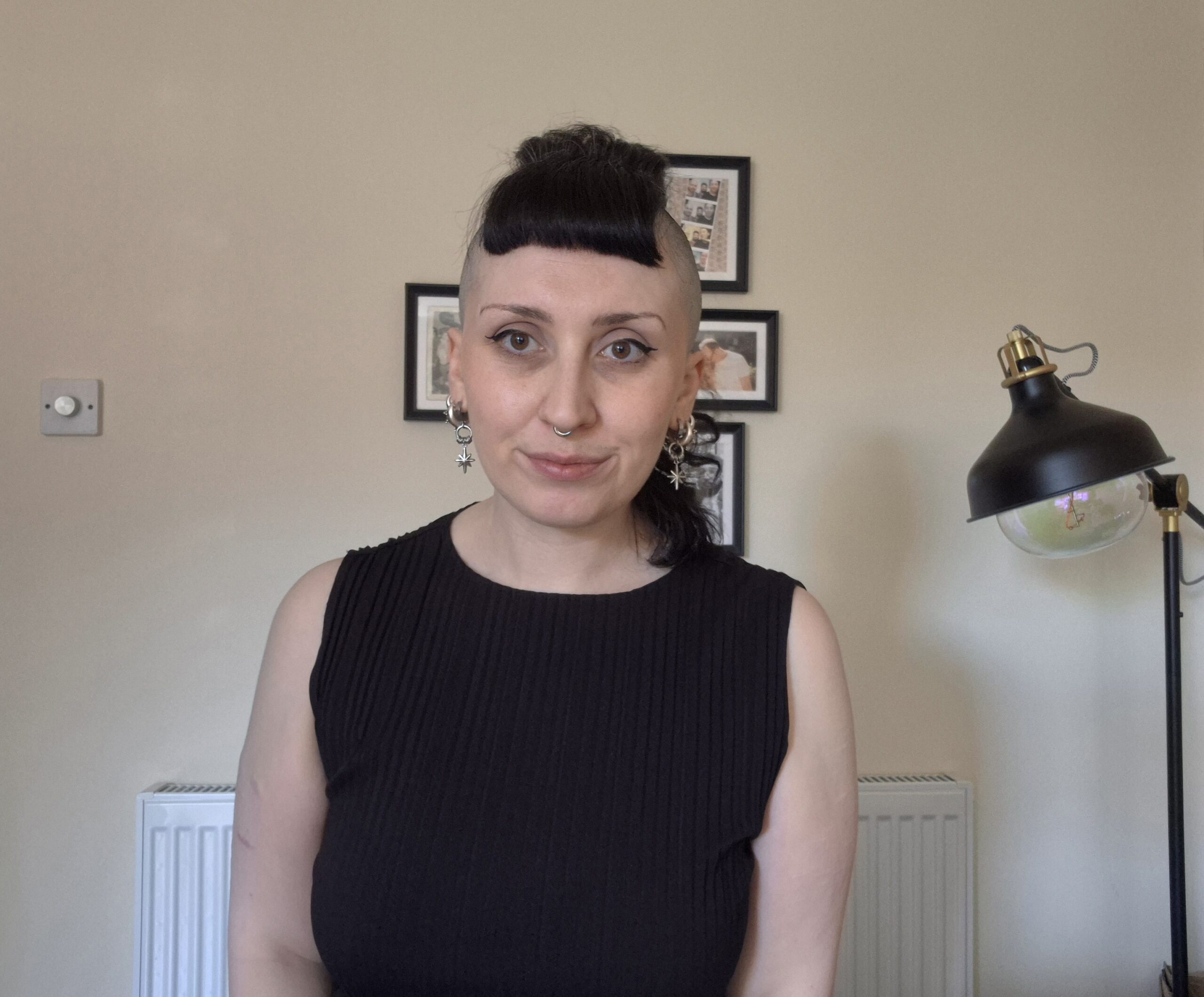 Seb is a white non-binary person with curly black hair, shaved sides and wears silver jewellery.