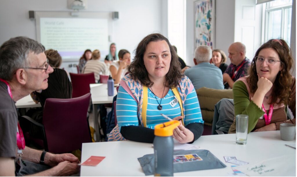 Woman in striped blue shirt speaks to the group of people at the table.